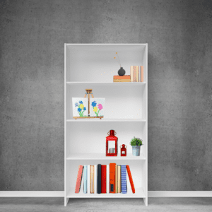 A white painted bookshelf sitting on a gray floor, in front of a gray wall. The top shelf of the book shelf has various colored books, the 2nd shelf has two paw print painted pictures, the 3rd shelf has various knick knacks and the bottom shelf has an assortment of books.