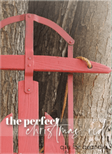 A red painted sled leaned up against a tree trunk with the words "the perfect christmas red" printed over it