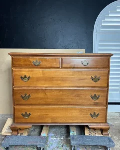 "Before" picture of brown wooden dresser sitting on furniture dollys in front of a black painted wall