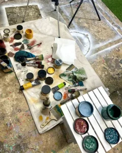 open jars of various colors of paint and various paint brushes sitting on top of a table