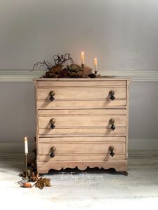 A wooden stained dresser sitting on a white floor, in front of a white wall