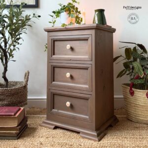 A nightstand stained with Charred Hickory Voodoo Gel Stain sits on a brown rug with plants and books around the nightstand