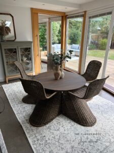 A round table and 4 wicker chairs painted with Umber Silk All-In-One Mineral Paint sits on a light colored rug in front of sliding glass doors that lead to a yard.