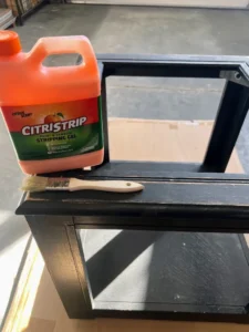 Black painted end table with jug of Citristrip and a paintbrush sitting on top of it