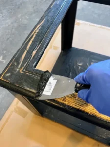 Hand holding a putty knife, stripping black paint off of an end table