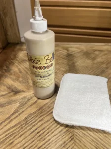 Au Naturel Voodoo Gel Stain sitting on top of a brown wooden table, next to a clean applicator pad