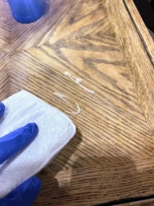 A hand rubbing Au Naturel VooDoo Gel Stain onto a wooden table with a white applicator pad