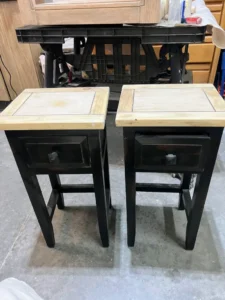 Two black painted end tables with light brown tabletops sit on a gray cement floor