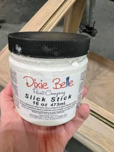 A hand holding a used jar of Slick Stick over a wooden end table