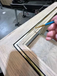 A hand holding a small paint brush over a wooden end table