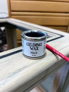 An open can of Black Gilding Wax and a red paint brush sitting on top of a wooden nightstand