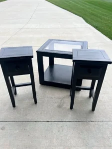 "Before" photo of 3 black painted end tables sitting on a cement ground with green grass in the background.