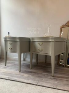 Two Dried Sage painted end tables sit on a brown wooden floor in front of a white painted wall